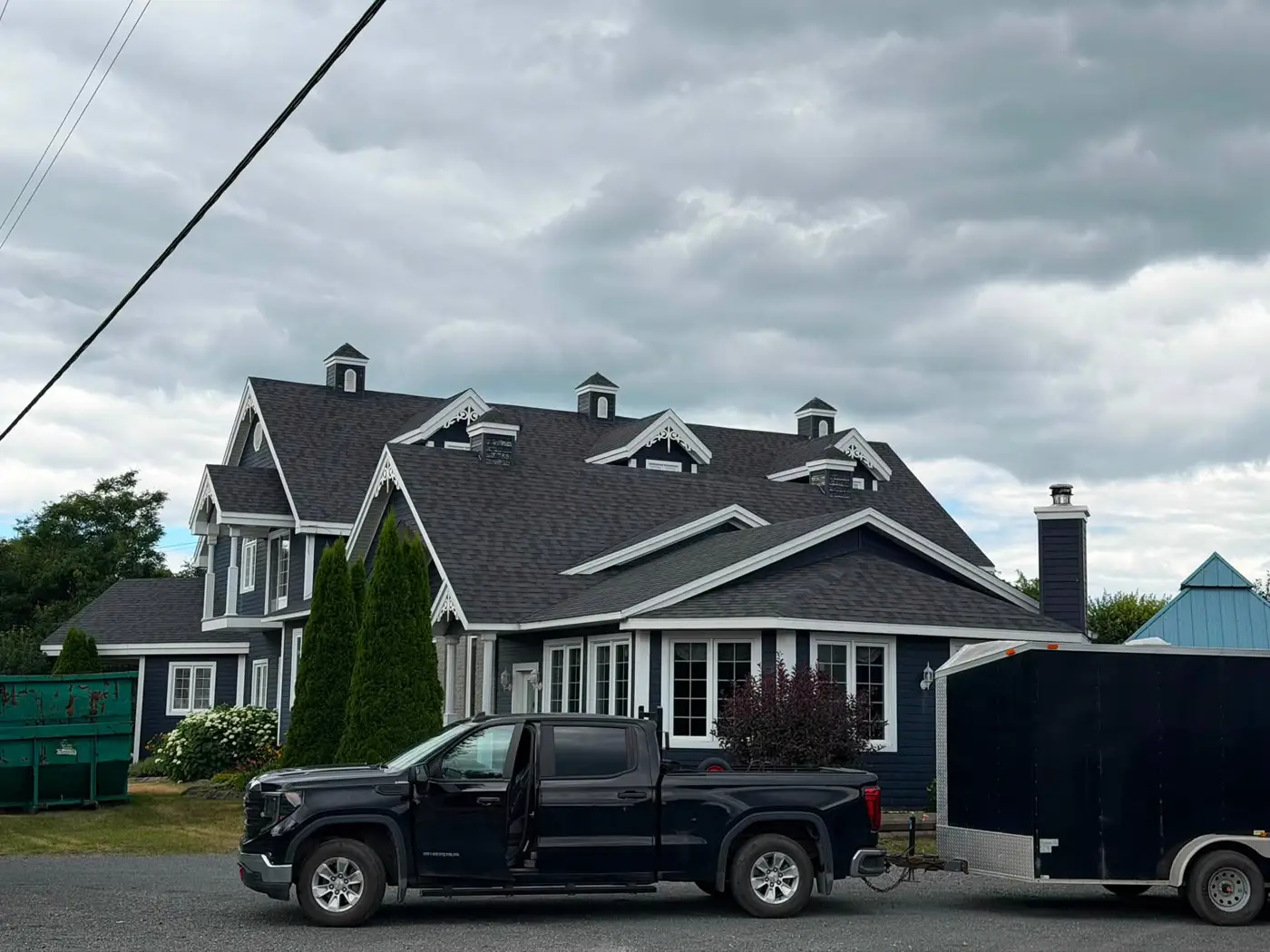 Camion et remorque de Toitures S. St-Onge devant une maison dont le toit vient d'être refait